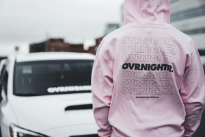 Man walking down the road wearing a pink sweater with hands in his pocket